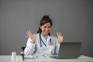 Young Asia lady doctor in white medical uniform with stethoscope using computer laptop talking video conference call with patient at desk in health clinic or hospital. Consulting and therapy concept. photo