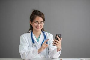 asiático hembra médico trabajo a hospital oficina escritorio dando paciente conveniencia en línea Servicio consejo, sonriente escribir un prescripción orden médico con teléfono inteligente, salud cuidado, prevenir enfermedad concepto. foto