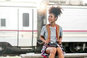 Young Asian African woman traveler with backpack in the railway train station, traveler girl walking stand sit waiting take a picture on railway platform train station. High quality photo