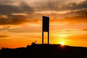 a sign on top of a hill with the sun setting behind it photo