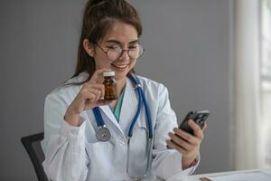 Asian female doctor work at hospital office desk giving patient convenience online service advice, smiling write a prescription order medical with smartphone, health care, preventing disease concept. photo