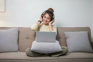 Portrait of Young Asian woman enjoy listening to music with headphones and using laptop, happy and relaxing time photo