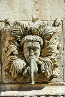 a stone face with a green pipe coming out of it photo