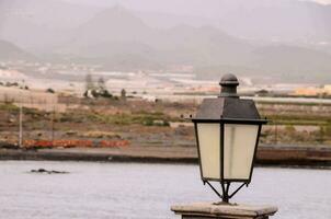 a street lamp near the ocean with mountains in the background photo