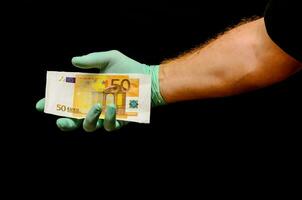 a person in a black shirt and green gloves holding a bank note photo
