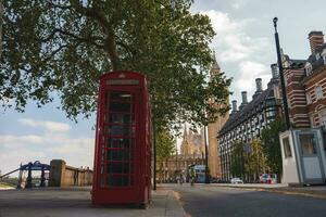 Empty red telephone booth and tree on sidewalk with famous Big Ben in background photo