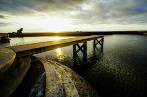 a pier at sunset with the sun shining through the clouds photo