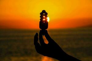 a person holding up a light bulb in front of the sunset photo