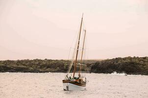 a sailboat in the ocean near rocky shore photo