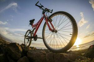 un bicicleta es estacionado en un rocoso playa a puesta de sol foto