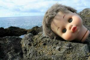 a doll head laying on the rocks by the ocean photo