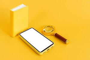 Small book, magnifying glass and smart phone, on yellow background. Online education. E-learning. photo