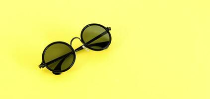 Stylish black sunglasses isolated on yellow background, top view. Summertime concept. photo