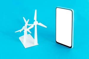 Wind turbines and smart phone on light blue background. Green eco friendly, ecology and environment conservation concept. Renewable energy for sustainable resources. photo