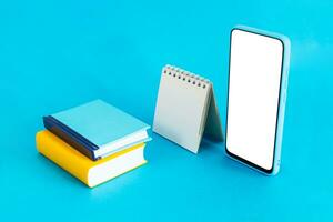 blanco calendario, cuaderno y inteligente teléfono, en ligero azul antecedentes. e-learning y calendario planificación concepto. foto