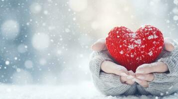 Female hands in knitted mittens with snowy heart against snow background photo