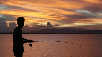 silueta de un pescador con un pescar varilla en el lago a puesta de sol foto