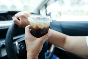 Asian woman driver hold drink in car, dangerous and risk an accident. photo