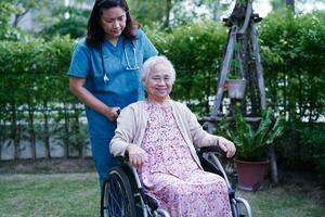 el médico ayuda a una anciana asiática con discapacidad a una paciente sentada en silla de ruedas en el parque, concepto médico. foto