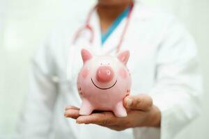 Asian woman doctor holding piggy bank, cost of treatment or education concept. photo