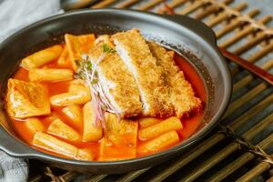 Tteokbokki, a spicy Korean dish of pork cutlets, vegetables, and fish cakes served on a black plate. photo