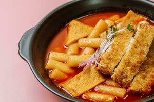 Tteokbokki, a spicy Korean dish of pork cutlets, vegetables, and fish cakes served on a black plate. photo