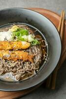 A summer dish of cold wheat noodles with fried shrimp in a black bowl photo