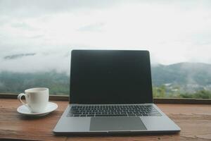 Computer Monitor, Keyboard, coffee cup and Mouse with Blank is on the work table at the sky mountain river and trees front view background. photo