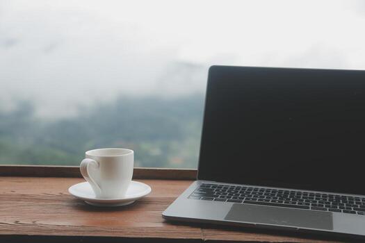 computadora monitor, teclado, café taza y ratón con blanco es en el trabajo mesa a el cielo montaña río y arboles frente ver antecedentes. foto