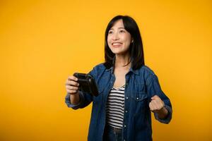 Portrait young asian woman with happy success smile wearing denim clothes holding joystick controller and playing video game. Fun and relax hobby entertainment lifestyle concept. photo