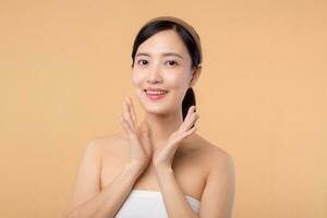 Beautiful girl asian model touching fresh glowing hydrated facial skin on beige background closeup. Beauty face young woman with natural makeup and healthy skin portrait. Skin care concept photo