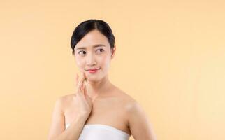 Beautiful girl asian model touching fresh glowing hydrated facial skin on beige background closeup. Beauty face young woman with natural makeup and healthy skin portrait. Skin care concept photo