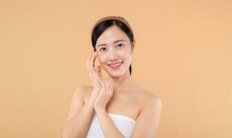 Beautiful girl asian model touching fresh glowing hydrated facial skin on beige background closeup. Beauty face young woman with natural makeup and healthy skin portrait. Skin care concept photo