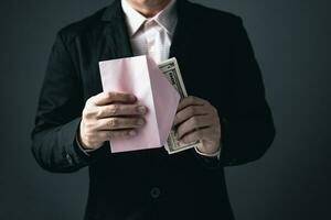 A male businessman in a black suit is bringing cash banknotes into paper envelopes, money and investment ideas or payment. photo