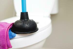 A serviceman is repairing a toilet with a hand plunger caused by a clogged toilet. photo