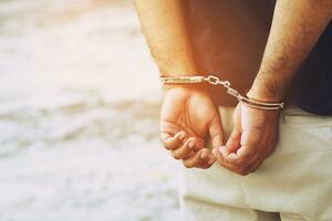 Arrest the offender. Prison male criminal standing in handcuffs with hands behind back. photo