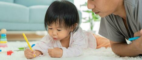 contento Asia padre jugando aprendizaje pintar para pequeño niño. gracioso familia es contento y emocionado en el casa. madre y hija teniendo divertido gasto hora juntos. día festivo, actividad foto