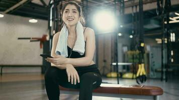 joven deportivo mujer auriculares escuchando a música en teléfono inteligente en gimnasia. descanso después difícil ejercicio. video