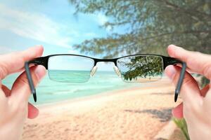 Female hand holding glasses focus mirror lens on sand sea travel trip. photo