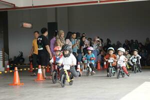 Depok-Indonesia, 29 07 2023 - Kids from 2-5 years old races on balance bike in a parking area, with parents on the back. photo