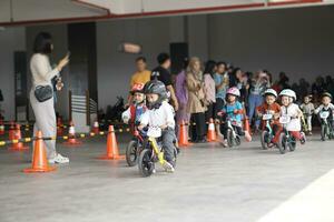 Depok-Indonesia, 29 07 2023 - Kids from 2-5 years old races on balance bike in a parking area, with parents on the back. photo