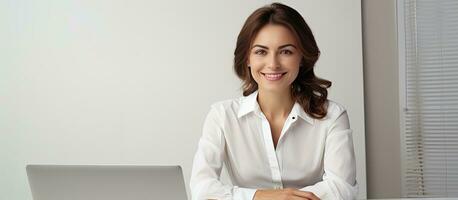 caucásico mujer trabajando felizmente a escritorio con ordenador portátil en blanco camisa foto