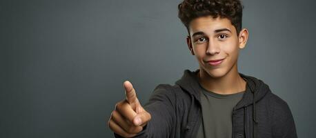 Smiling teenage boy pointing upward in a portrait on a grey background photo