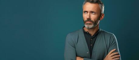 Middle aged man with serious expression standing against blue studio wall looking sad holding back emotions contemplating a problem with empty space photo