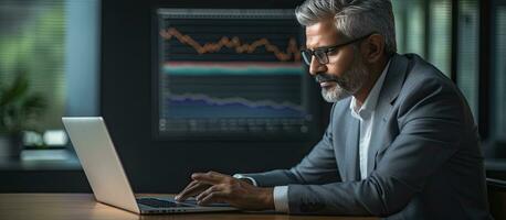 Mature CEO of Indian or Latin origin using laptop in contemporary office analyzing online data and devising tech strategy photo