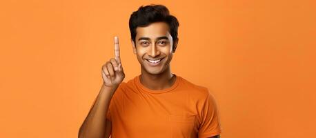 The attractive Indian man is happily posing and showing a thumbs up isolated on an orange backdrop for advertisement photo