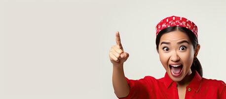 Asian woman in red kebaya and flag headband pointing at empty space above her on white background looking enthusiastic photo