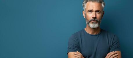 Middle aged man with serious expression standing against blue studio wall looking sad holding back emotions contemplating a problem with empty space photo