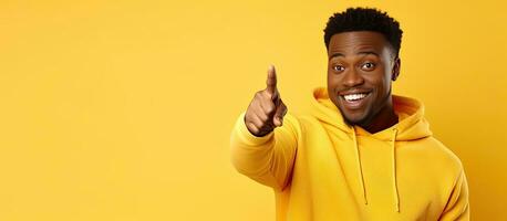 Young African American man in bright yellow hoodie happily pointing at blank space for online ad photo