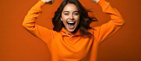 Enthusiastic young woman playfully imitates a rider dances energetically and happily points upwards dressed casually posing in a studio with an orange bac photo